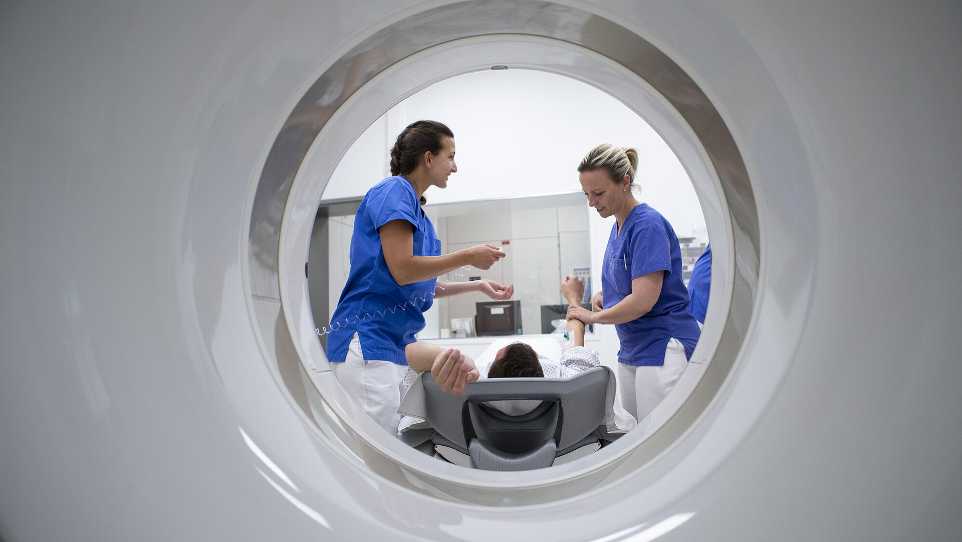 Blick durch einen Tunnel auf 2 Schwestern und einen Patienten auf einer Trage