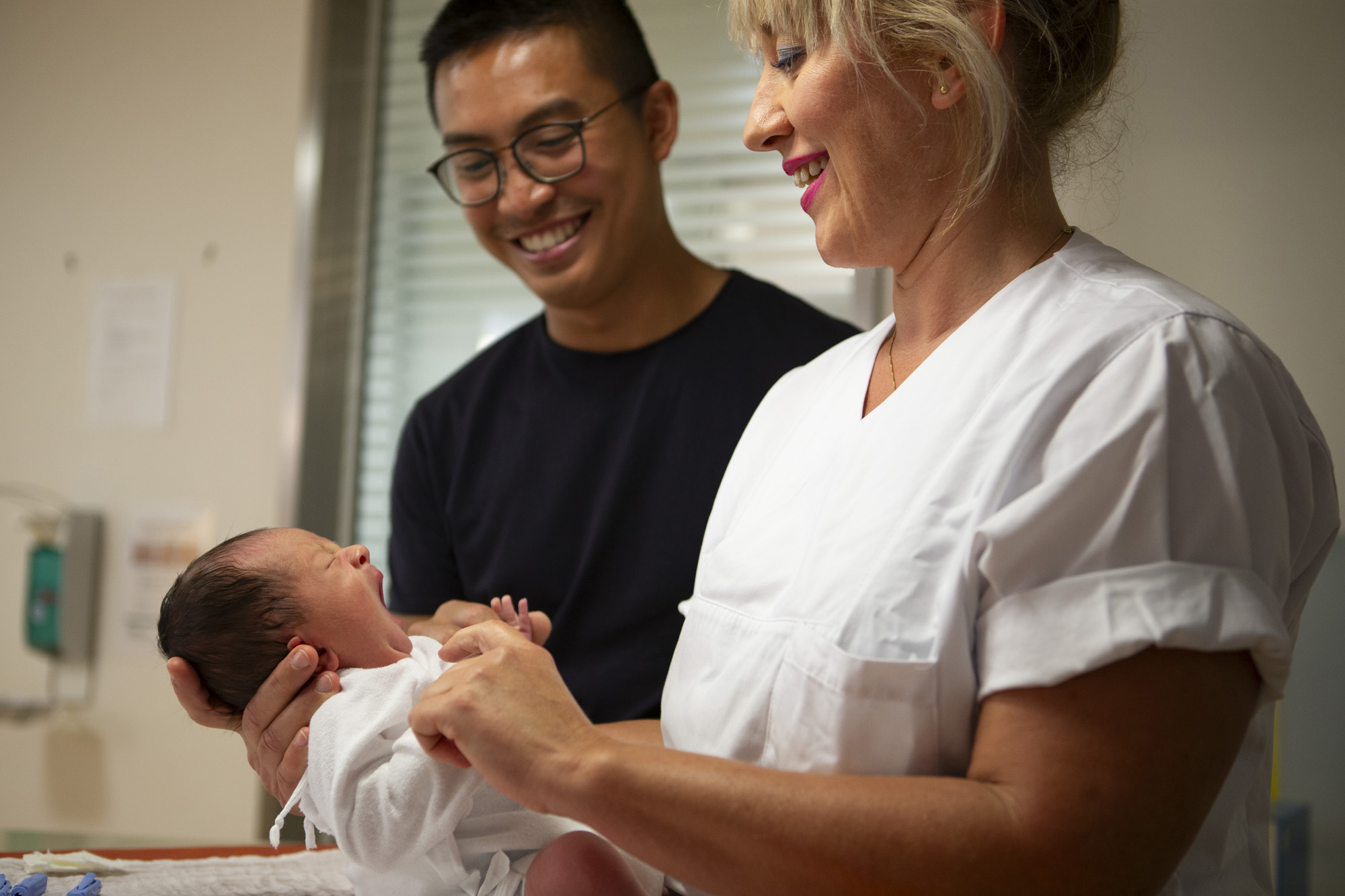 Eine Schwester hält ein Baby hoch während der Vater lächelnd daneben steht